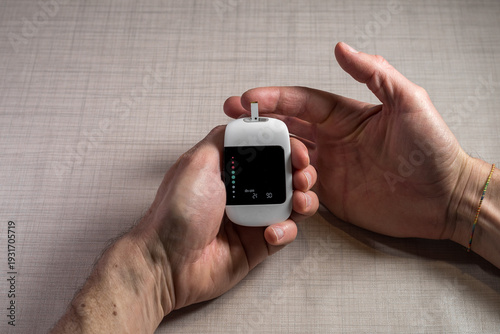 Close up of a man hands using a digital glucose meter to check blood sugar levels at home. Concept of diabetes management, medical self-testing, and healthcare monitoring for a healthy lifestyle.