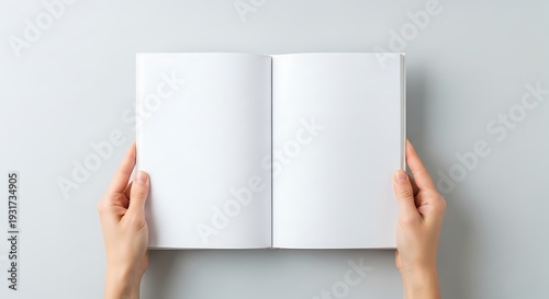 Person holding open blank book with both hands on white surface