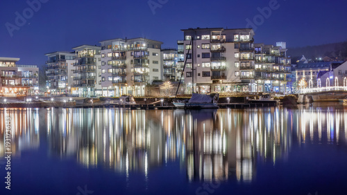 Blue hour northern character illuminated waterfront architecture mirrored in river at night in Porsgrunn Norway capturing structured facades and Scandinavian urban clarity.