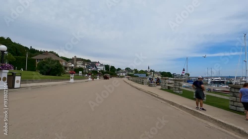 POV cycling past Mackinac Island harbor. A smooth shot moving past the marina’s sailboats and yachts, with sparkling Lake Huron and historic waterfront buildings in the background.