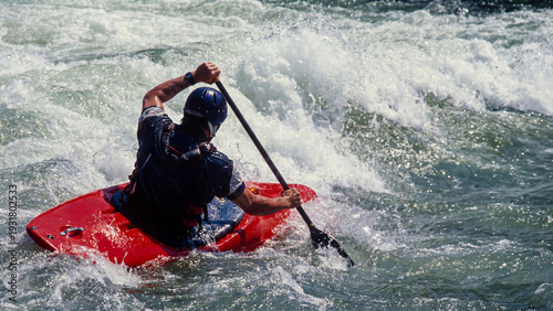 Whitewater kayaker navigating powerful rapids, extreme river paddling action. Crashing waves and splashing water. Control and adrenaline in extreme sport concept.
