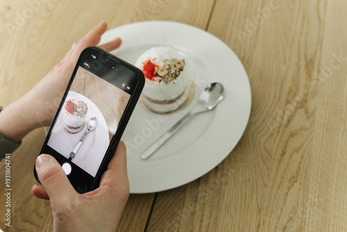 Close-up of hands holding smartphone and taking picture of dessert in cafe. Concept of social media, food blogging, influencer lifestyle and digital content creation.