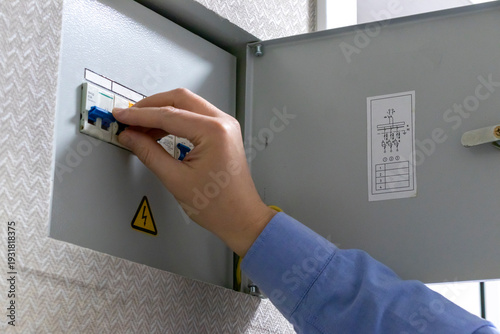 A man checks an indoor circuit breaker box. Electric