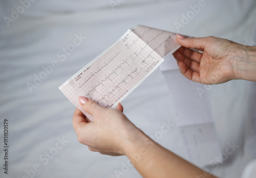 Hands with electrocardiogram paper showing heart rhythm data. Heart disease prevention and medical checkup theme.