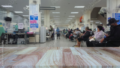 Empty wooden table top with blurred background of patients waiting to see doctor in hospital or clinic. Mock up for display of health and medical products.