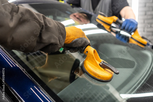 Automobile special workers replacing windscreen or windshield of a car in auto service station garage. Glass of the car, removed with the help of professional suction cups. The process of car repair.