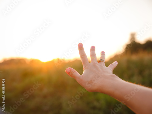 Soft evening light bathes golden field as woman's hand gently moves through tall grass, capturing sense of freedom, nature, and serenity. Warm sunset hues create peaceful, dreamy countryside atmospher