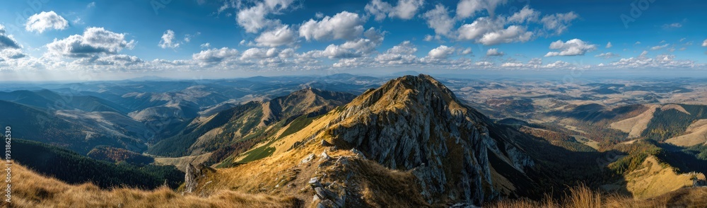 Fototapeta premium Panoramic View of Majestic Mountain Landscape Under a Vibrant Blue Sky with Fluffy Clouds.