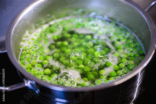 Fresh green peas boiling in a stainless steel pot on a stovetop, with bubbling water and steam. Simple cooking process, healthy food preparation, and everyday kitchen scene.