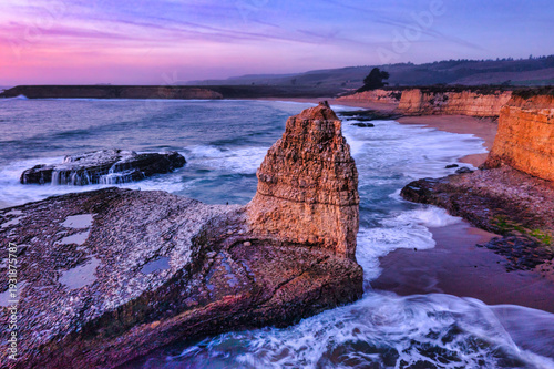 Rock formation at sunset on Four Mile Beach in Santa Cruz California with ocean waves swirling around coastal cliffs under a golden sky