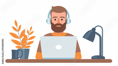 Bearded man working on laptop with headphones on at desk with plant and lamp