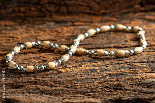 Pearl necklace, a beautiful, stage-prop pearl necklace positioned on very rustic wood against a dark background, selective focus.