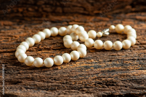 Pearl necklace, a beautiful, stage-prop pearl necklace positioned on very rustic wood against a dark background, selective focus.