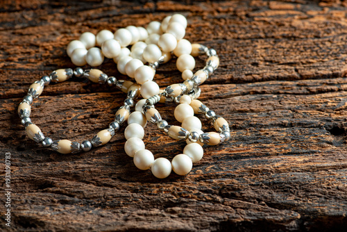 Pearl necklace, a beautiful, stage-prop pearl necklace positioned on very rustic wood against a dark background, selective focus.