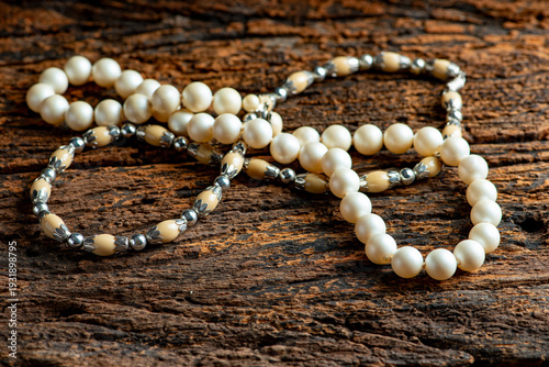 Pearl necklace, a beautiful, stage-prop pearl necklace positioned on very rustic wood against a dark background, selective focus.