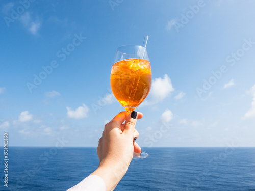 Hand holding a glass of drink against a bright blue sky. Refreshing cocktail moment, summer relaxation and a vacation vibe. Perfect for beverage, travel, and lifestyle marketing campaigns. Close-up