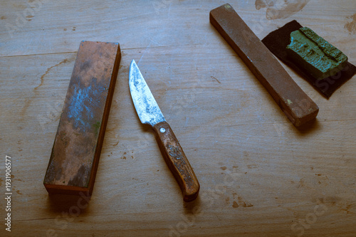 Vintage wooden handle utility knife with whetstone on rustic surface.