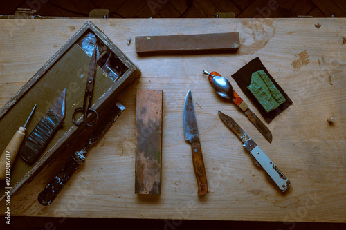 Collection of vintage hand tools and old knives in a wooden toolbox on a rustic workbench.