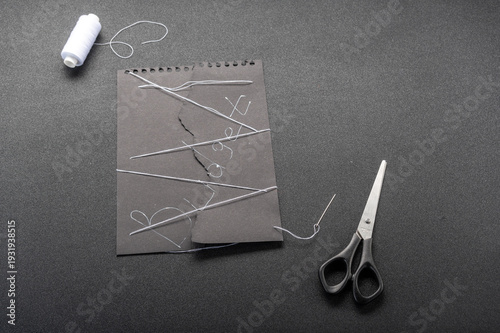 Broken budget concept. Torn black paper with Budget word sewn together with white threads on black background.