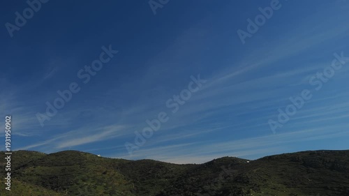 4K timelapse of rolling green hills in the Cyclades under deep blue sky with delicate horizontal cloud streaks. Minimal Mediterranean landscape with wide copy space and calm natural atmosphere. Ideal 