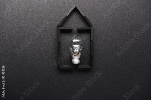 Minimalist flat lay of a domino house with a glass light bulb on a black background.
