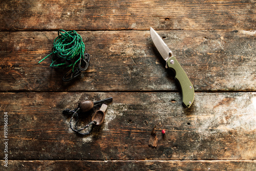 Survival tools: folding knife, jute rope, and flint fire starter on an old wooden table.