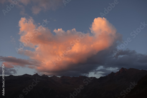 Big sunlit orange cloud over mountain silhouette at sunset, Vallelunga, Alto Adige Sudtirol, Italy