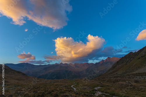 Sunset panorama of alpine stream with orange peaks and sunlit clouds background, Vallelunga, Alto Adige Sudtirol, Italy