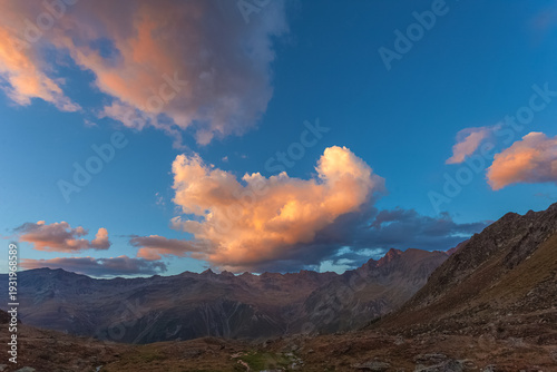 Alpine sunset panorama with orange sunlit clouds over mountains, Vallelunga, Alto Adige Sudtirol, Italy