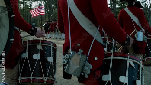 Revolutionary War soldiers in red coats marching with drums and a flag