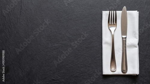 Minimalist Table Setting with Silver Fork and Knife on White Napkin over Dark Slate Background