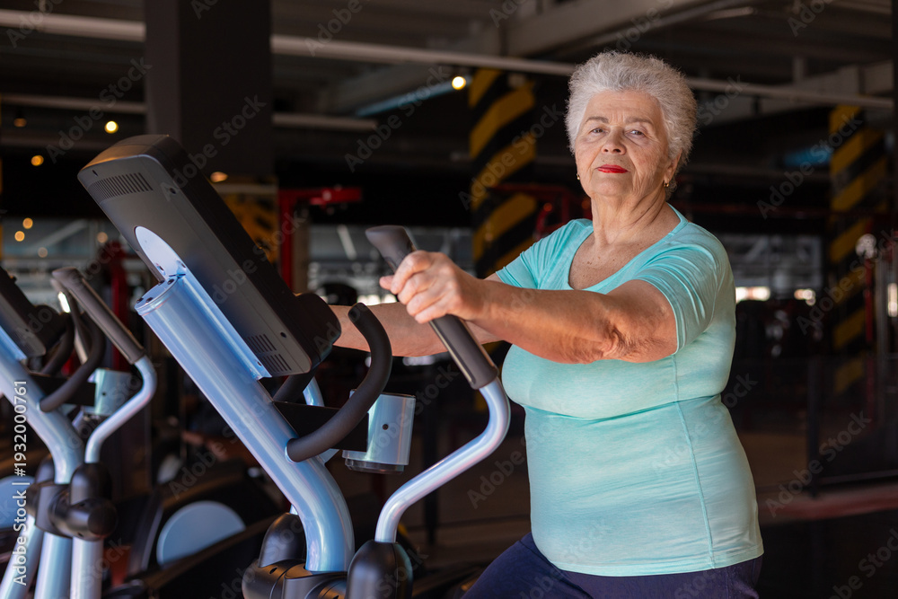 Fototapeta premium Active senior woman exercising on elliptical trainer in gym. Concept of menopause fitness, bone health, osteoporosis prevention and healthy aging. Mature woman maintaining strength and mobility 