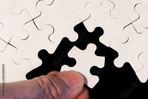 Close-Up of Hand Placing White Jigsaw Puzzle Piece Into Place on Black Background