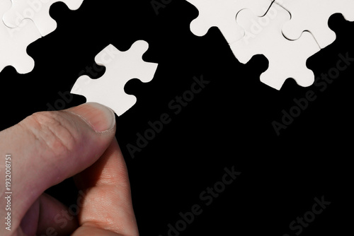 Close-Up of Hand Placing White Jigsaw Puzzle Piece Into Place on Black Background