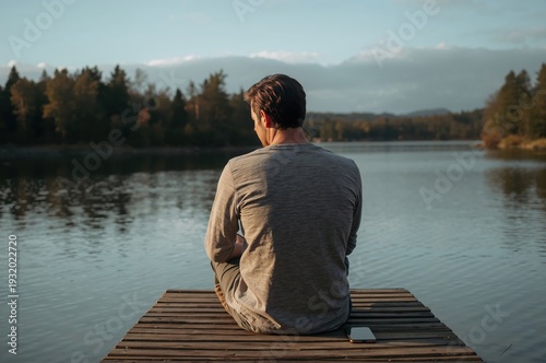 Wallpaper Mural Man reading quietly on wooden dock beside calm lake during peaceful golden hour evening Torontodigital.ca