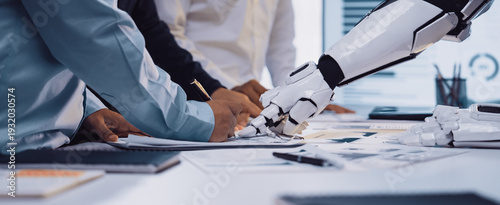 Obraz na plátně An engaging scene of collaboration in a modern office where human hands and a robot arm work together over documents, reflecting the future of innovative teamwork