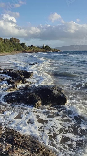 A lighthouse surrounded by rocks in a windy and choppy Aegean Sea. Akyarlar, Bodrum. Vertical video for social media. 