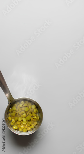 Metal ladle filled with simple split pea soup resting on the lower left edge of a large pale gray background, most of the space left empty as negative space for nutrition or budget cooking text.