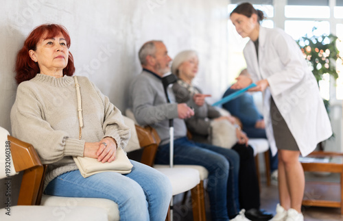 Fotografie Group of elderly people sitting in chairs in queue to see doctor, nurse talking