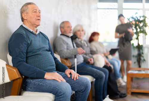 Foto Serious senior man calmly waiting in line at public healthcare facility before d