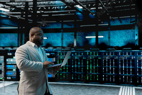 Data center software developer using laptop to protect servers from exploitable software vulnerabilities, auditing systems. African american server farm employee looking for bugs slowing down rigs
