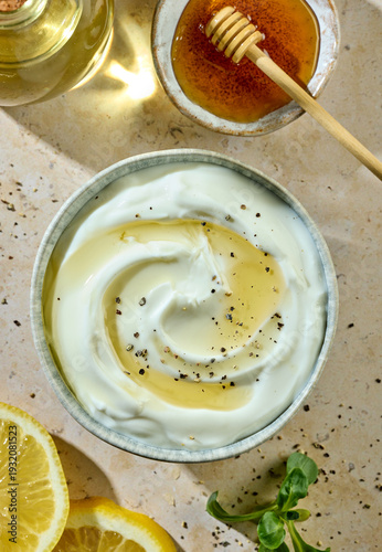 Greek yogurt bowl with honey and spices on sunny kitchen table with ingredients, top view
