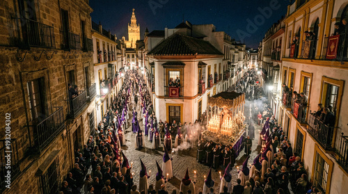 Procesión nocturna de Semana Santa en España con nazarenos de túnicas moradas y velas encendidas, acompañando un paso iluminado por cirios en calle histórica empedrada.