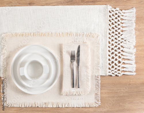 An empty white plate setting with a placemat situated on a light wood dining table, ready for a meal