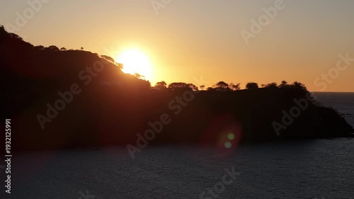 Aerial movement revealing sunset behind tropical cliff