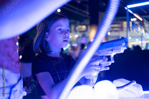 Girl playing laser tag shooting game in neon lit arcade entertainment center with bright glowing lights and immersive gaming atmosphere 