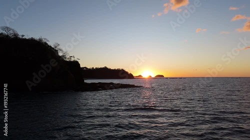 Aerial reveal of sunset behind coastal cliff and islands