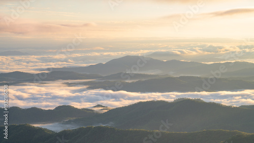 Low lying clouds drift between rolling Appalachian mountain ridges at golden sunrise, creating layers of misty peaks and valleys in soft morning light with peaceful, serene atmosphere