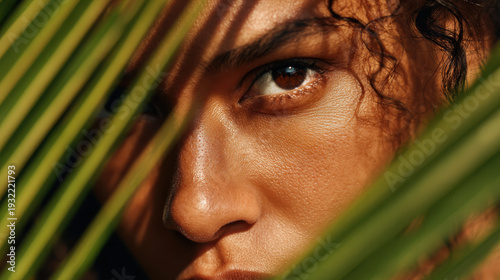 Close up of a womans eye looking through tropical palm leaves for exotic summer vacation and beauty concepts