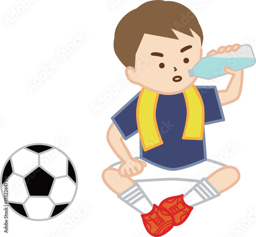 首にタオルを巻いて地面に座って水分補給をするサッカー少年